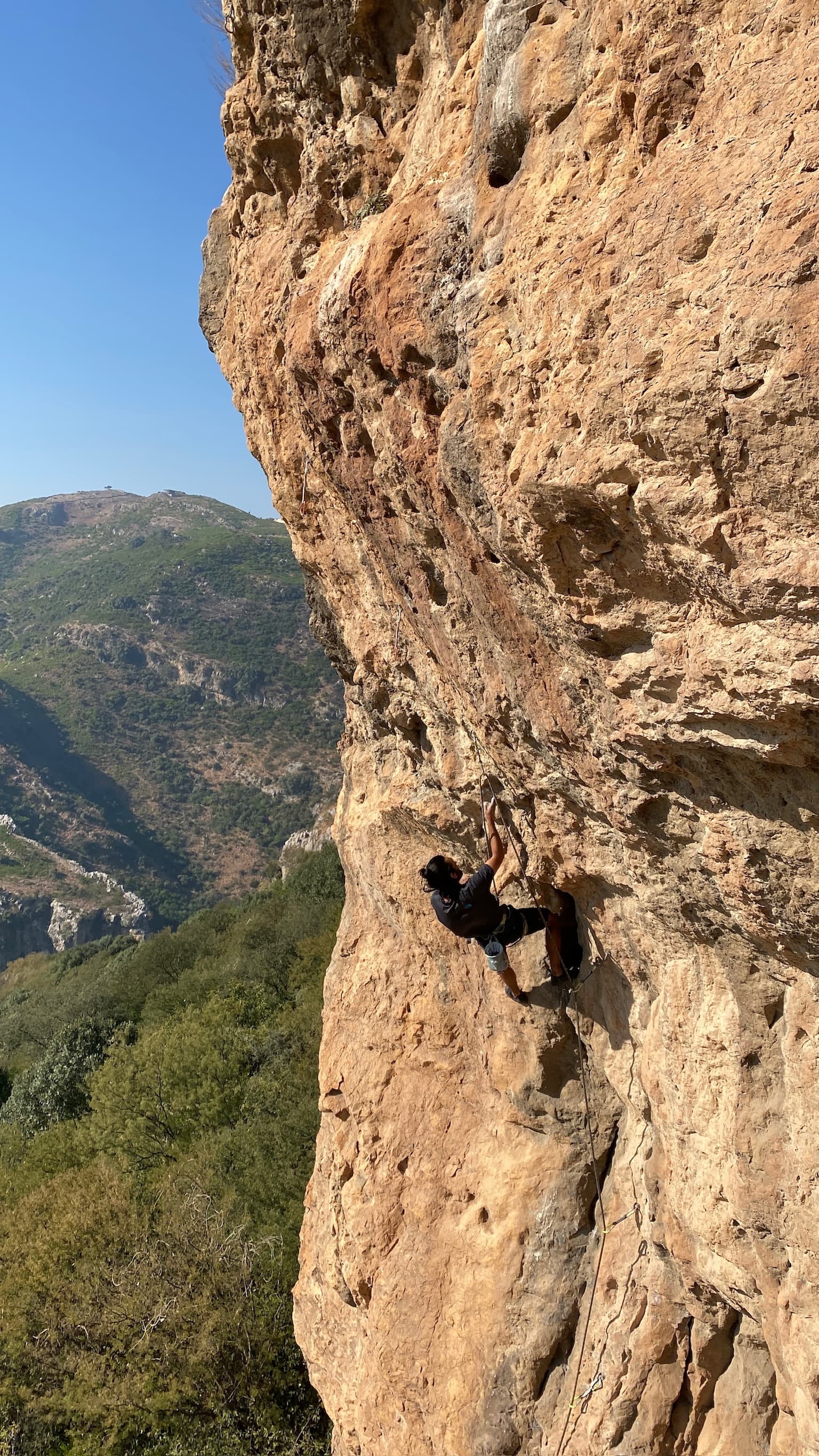 Side view of a lead climb on ochre rock above green hills